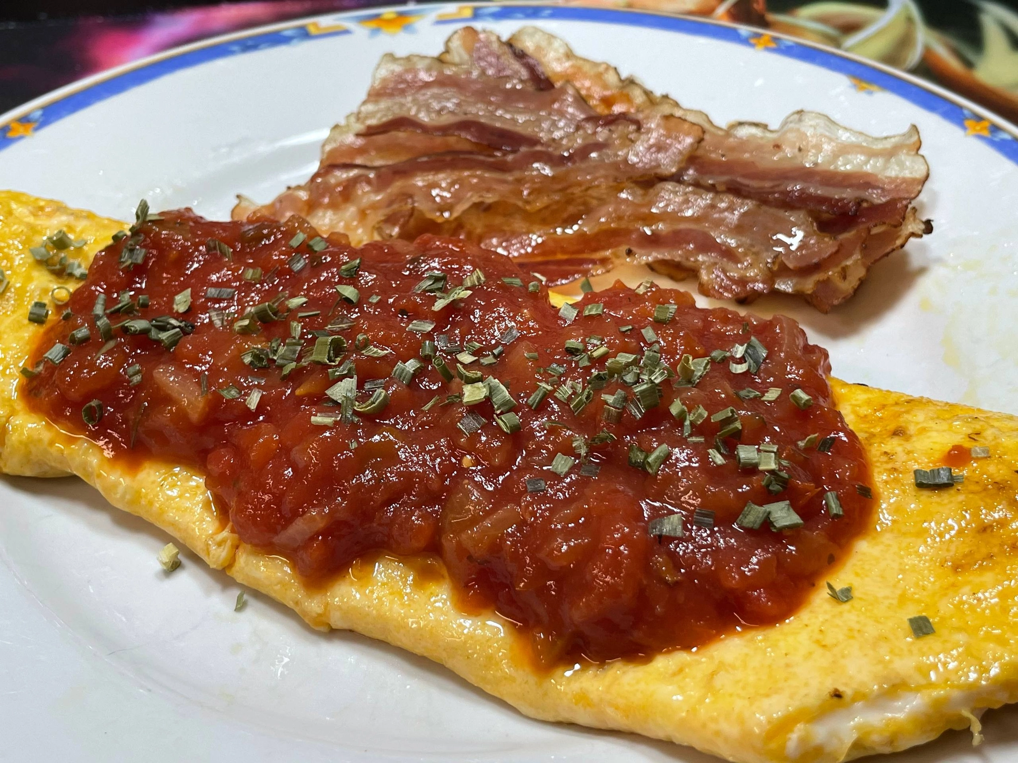 a plate with an omlette and bacon on it. the omlette is covered in salsa and chives
